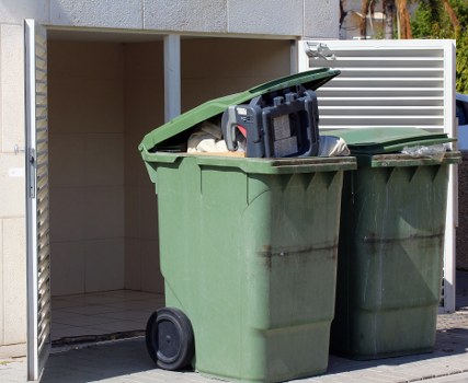 Front view of a commercial waste collection vehicle parked in Mill Hill near a business premises.